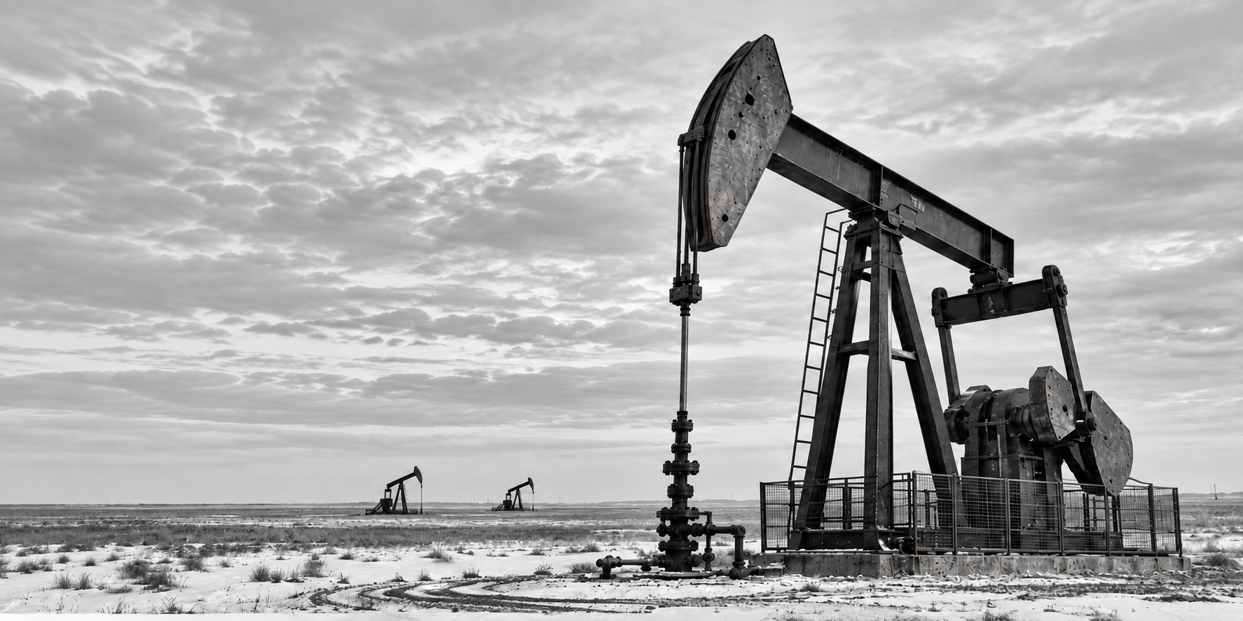 Oil pumpjacks on a snow-covered prairie beneath a cloudy sky